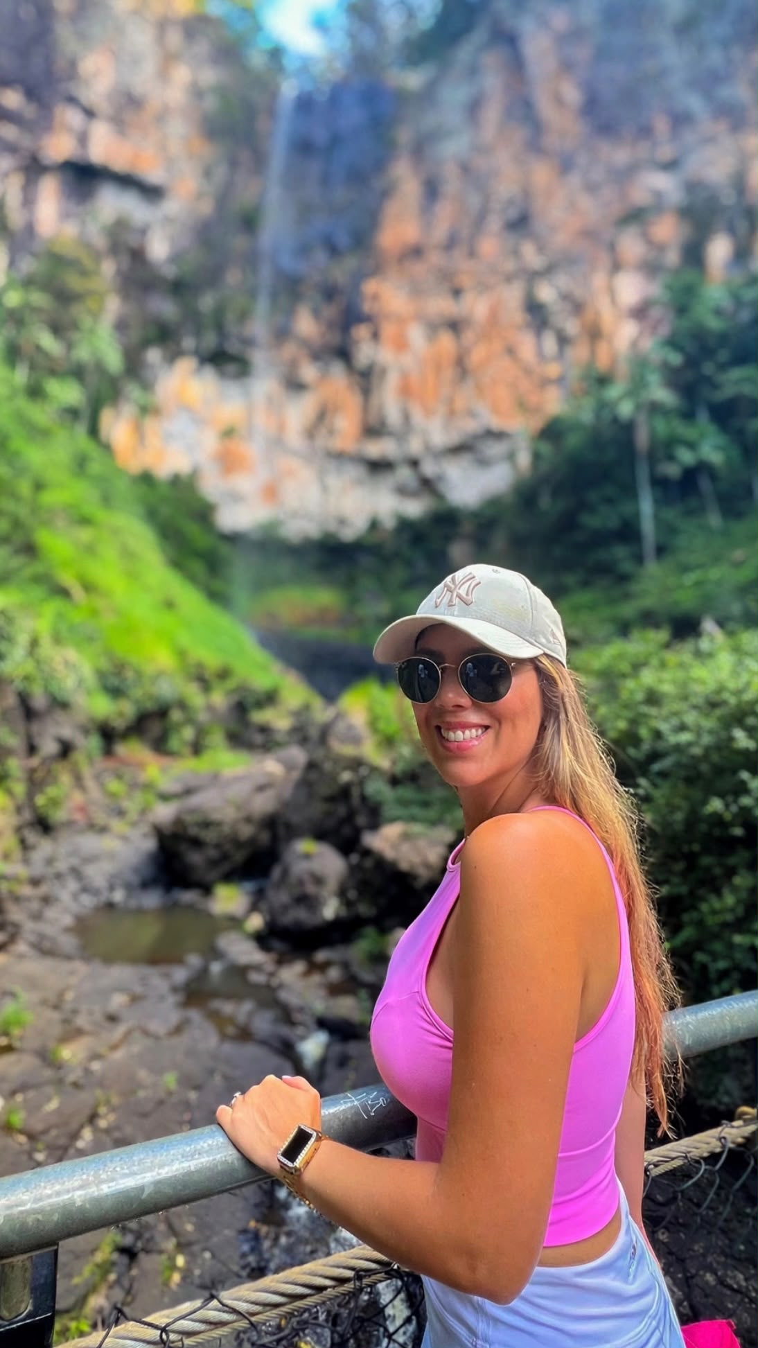Priscila sorrindo em frente a uma cachoeira na floresta