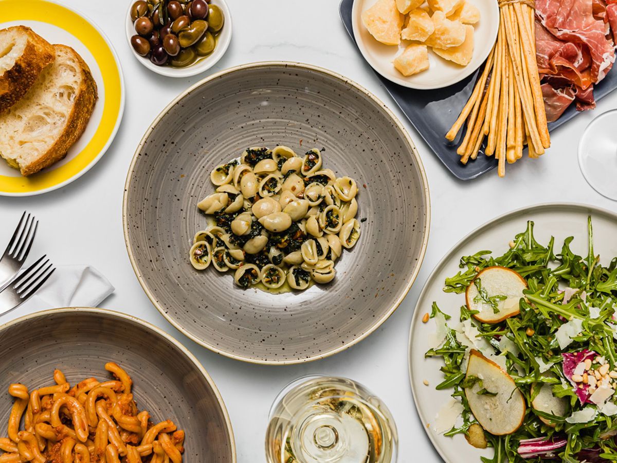 Mesa de restaurante italiano com massas, salada, pães e vinho