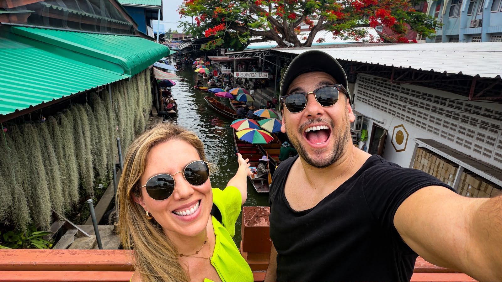 Nós no mercado flutuante, com barcos e guarda-chuvas coloridos ao fundo